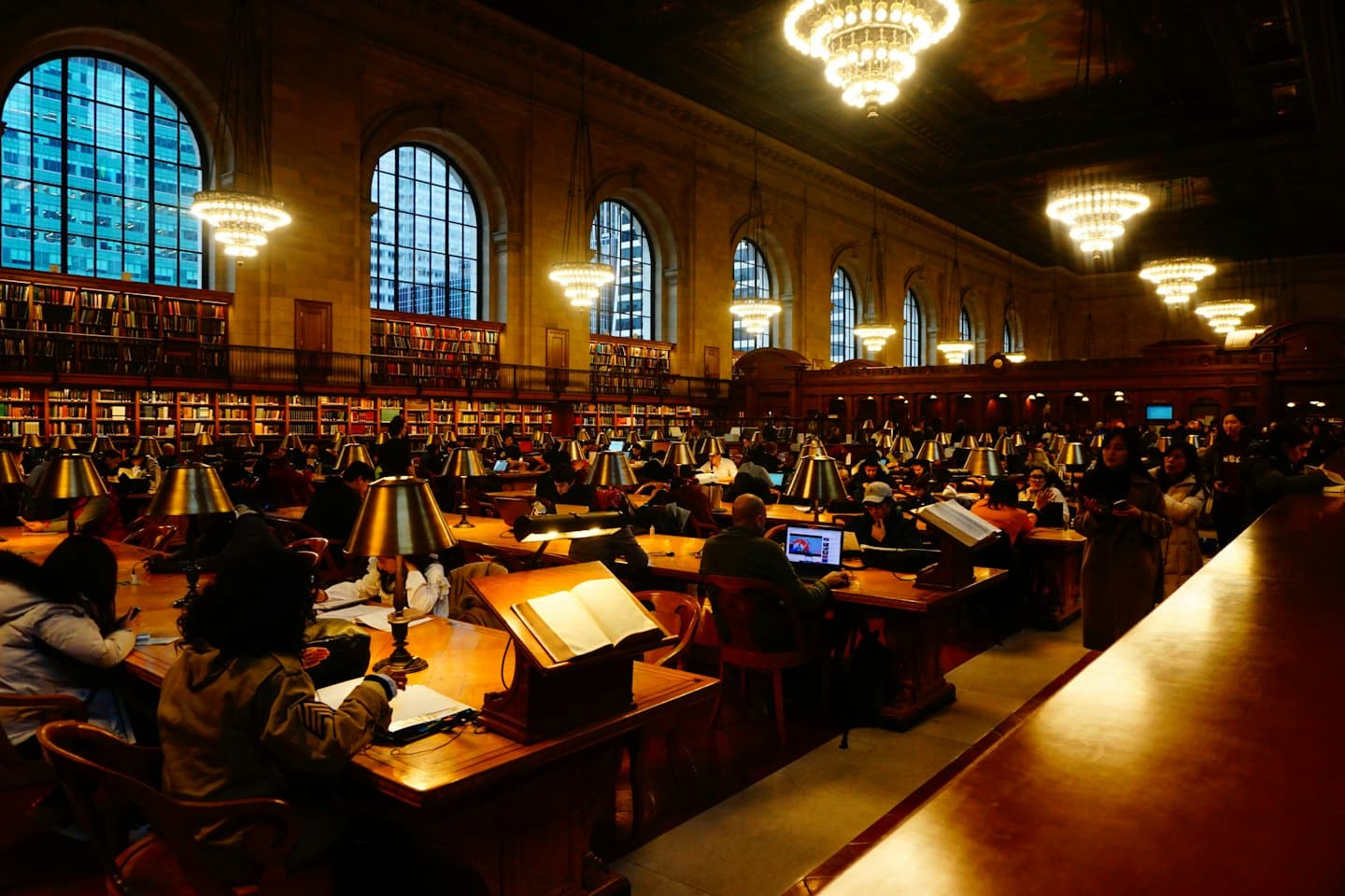 Menschen studieren in einem großen Bibliothekslesesaal mit hohen Bücherregalen.